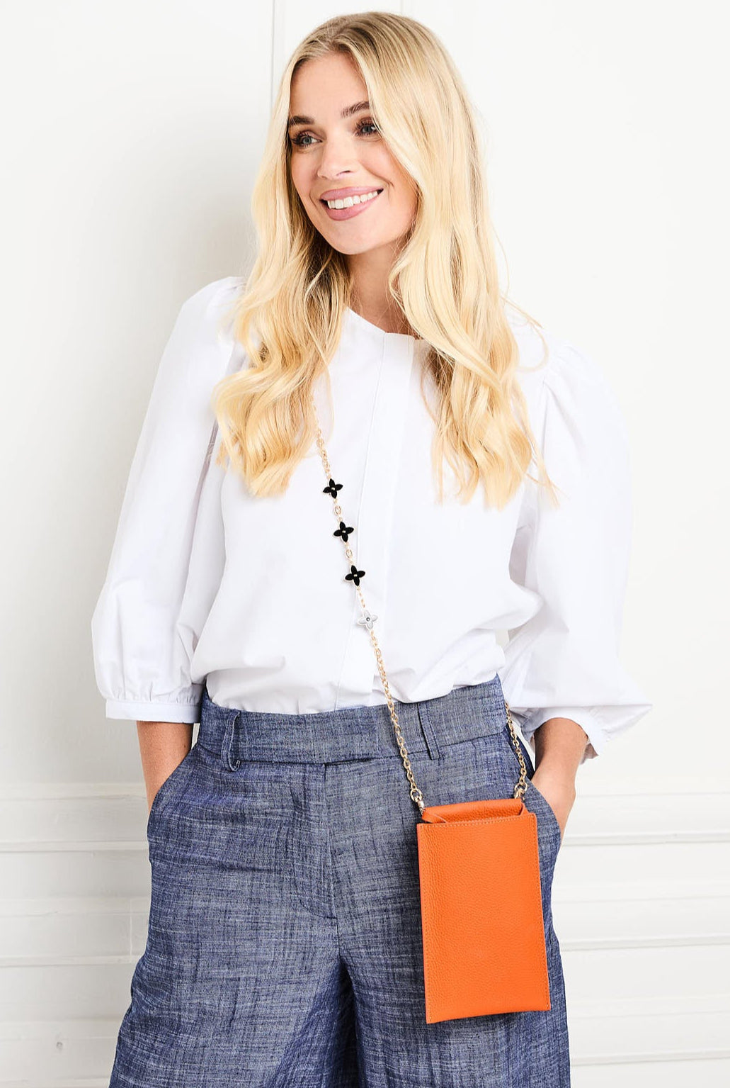 Image of a Model displaying the Orange Leather Phone Pouch for Women by Elie Beaumont with Daisy Chain Lanyard Strap