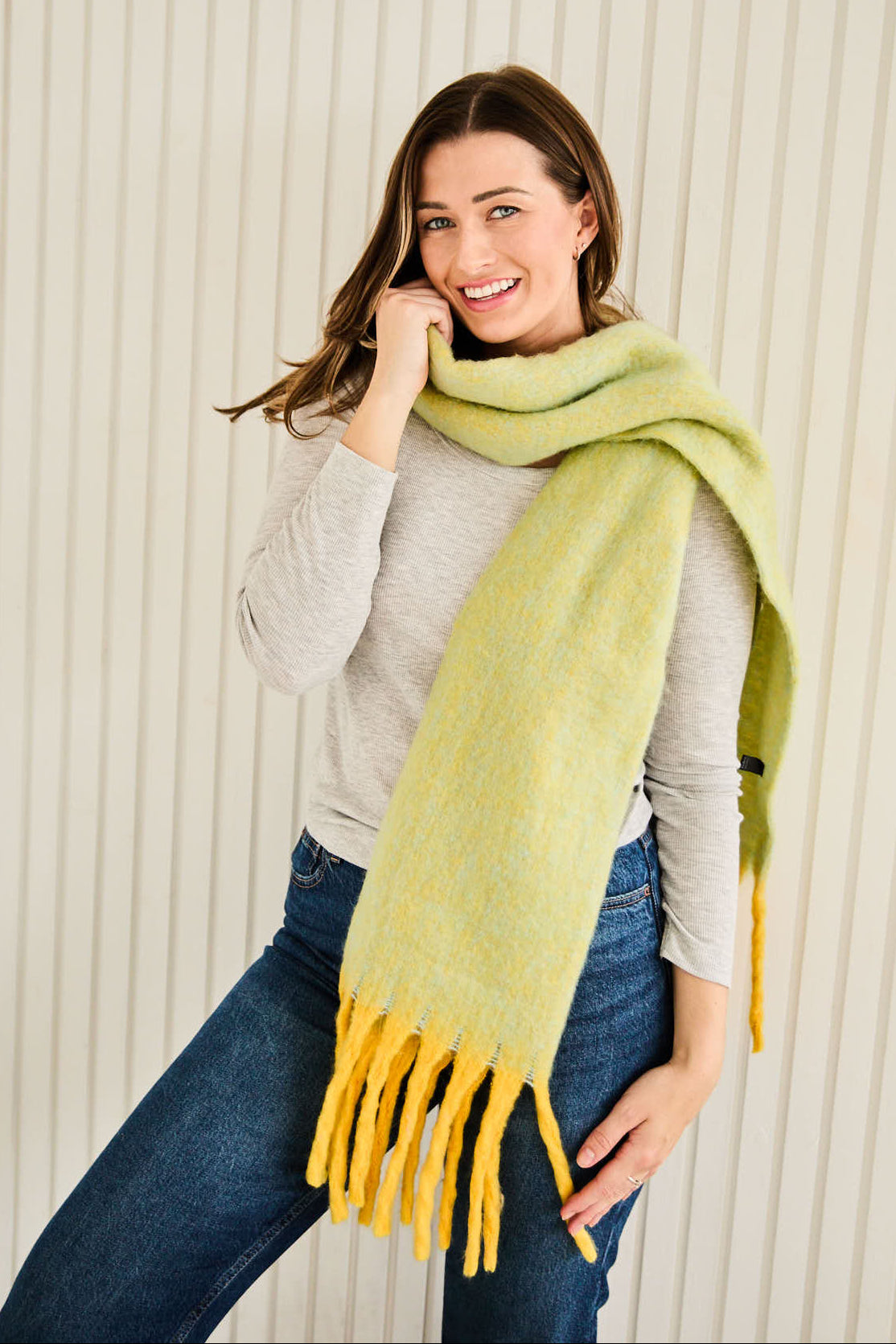 Woman wearing a Eiie Beaumont lime green scarf with yellow fringe against a beige background